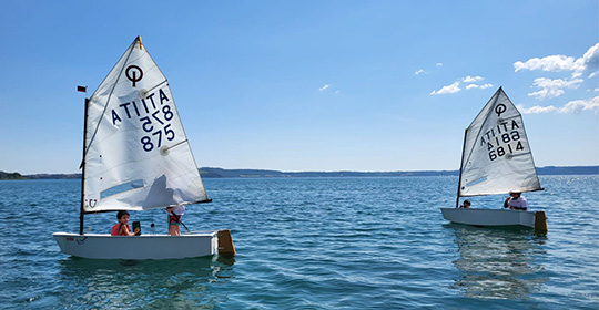 Bambini in barca a vela Optimist sul lago di Bracciano